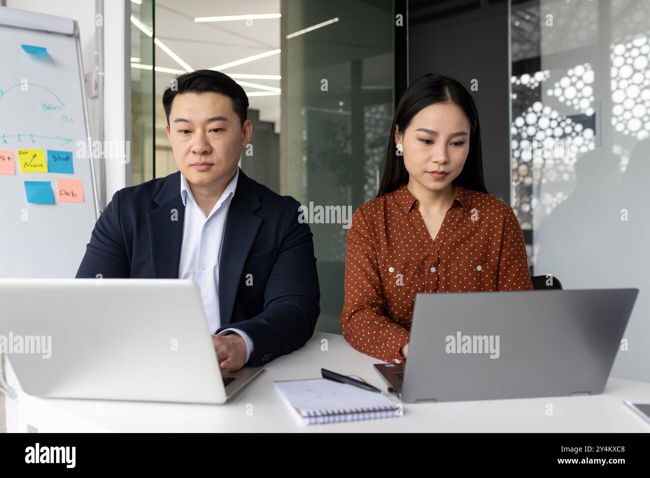 Professionnels asiatiques travaillant sur des ordinateurs portables dans le bureau contemporain. Collaboration et concentration sur les tâches numériques, démontrant le travail d'équipe et la productivité. Banque D'Images