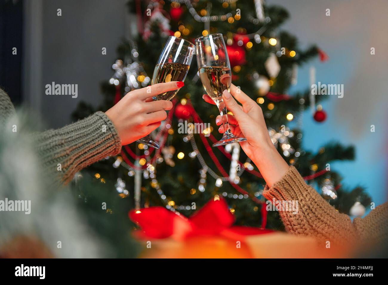 Deux femmes flânent des verres de champagne devant un sapin de Noël décoré, célébrant les fêtes ensemble. Banque D'Images