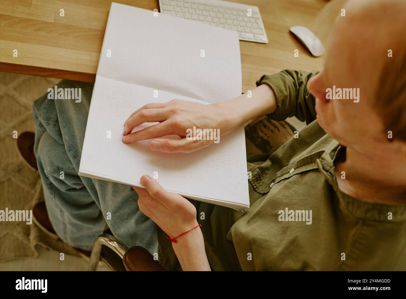 Plan haut en bas d'un homme méconnaissable avec une déficience visuelle assis à une table en bois et lisant un livre en braille Banque D'Images