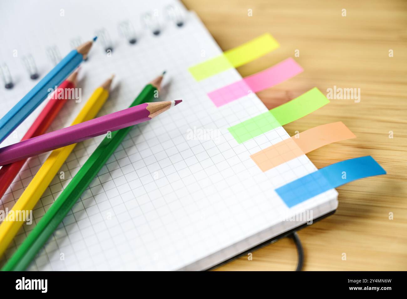 Crayons de couleur sur une partie d'un cahier en spirale avec du papier carré et étroit post sur un bureau en bois, bureau créatif ou fournitures scolaires, espace de copie Banque D'Images