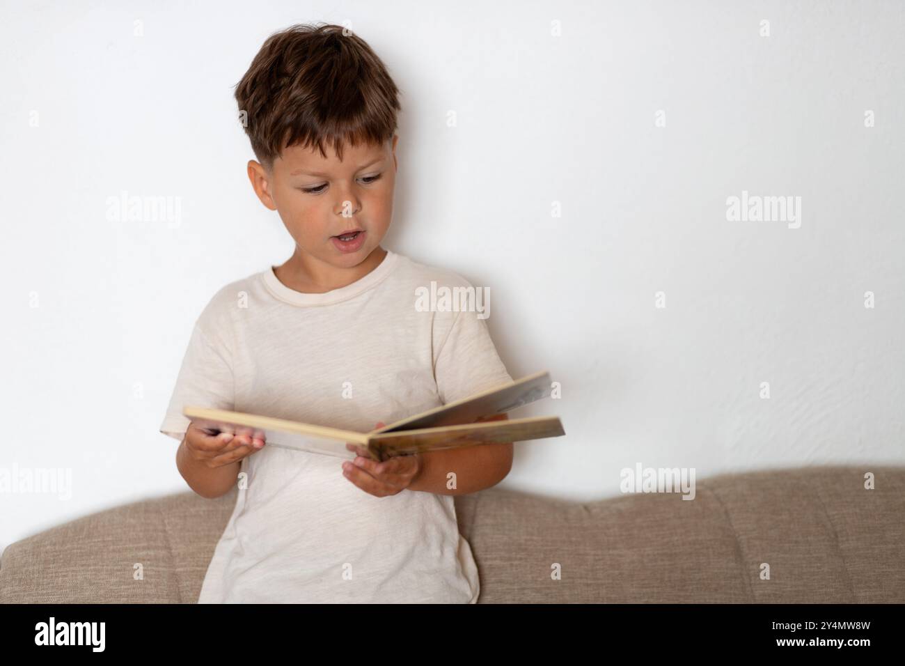 Un enfant de six ans lit avec enthousiasme à haute voix debout sur un canapé. Banque D'Images