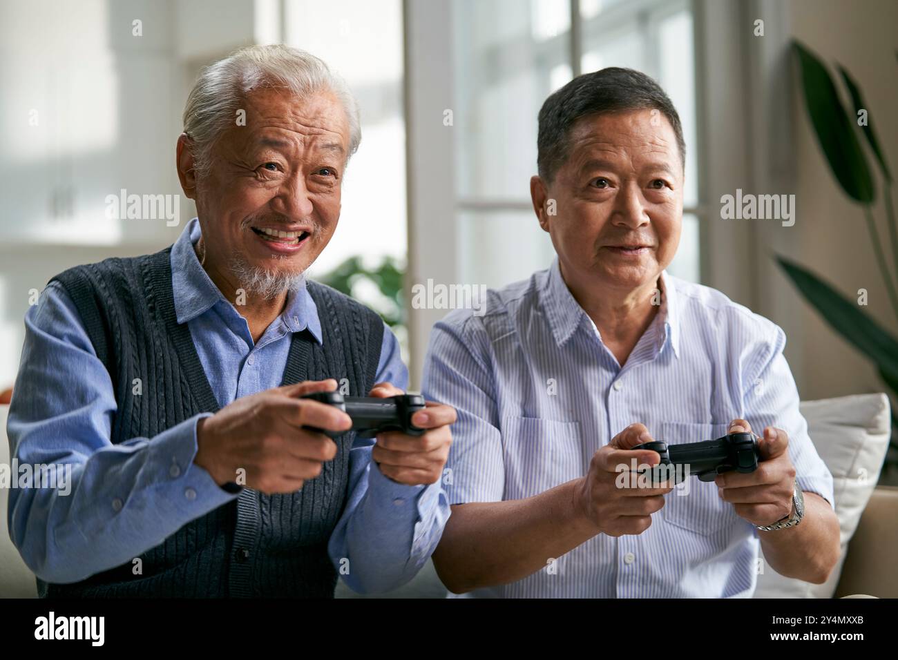 deux heureux hommes asiatiques seniors assis sur le canapé à la maison jouant au jeu vidéo ensemble Banque D'Images