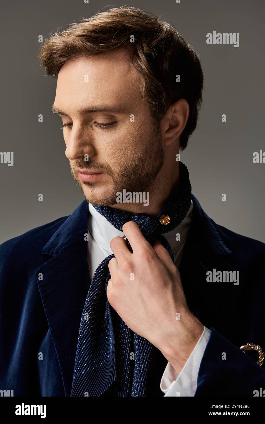 Un homme dapper dispose soigneusement son écharpe tout en mettant en valeur un style raffiné dans une lumière tamisée. Banque D'Images