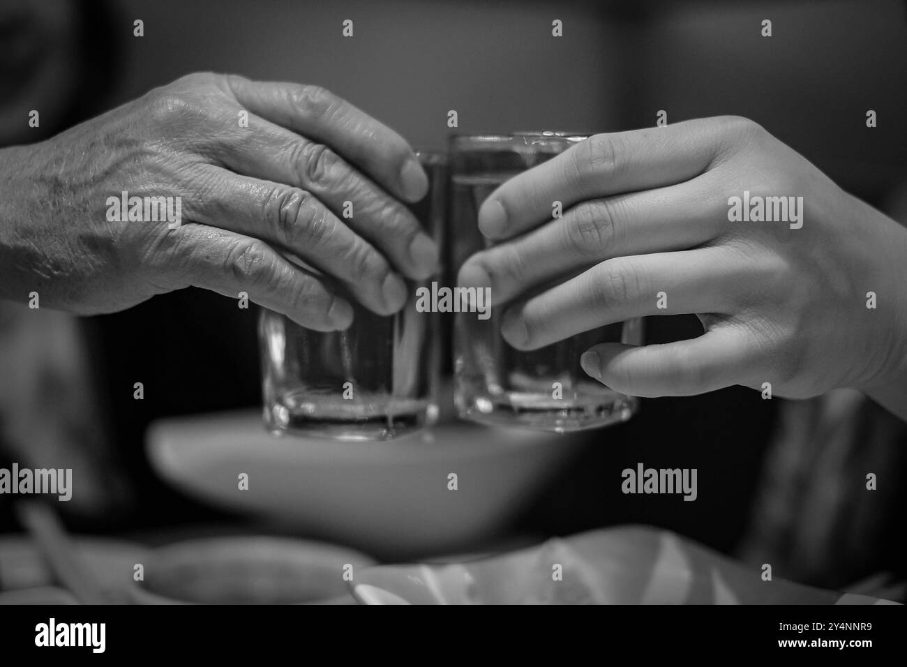 Lunettes à deux mains avec shot de whisky à la maison. Les mains d'un vieil homme et d'un jeune homme claquent des verres de vodka. Photo noir et blanc. Deux verres Banque D'Images