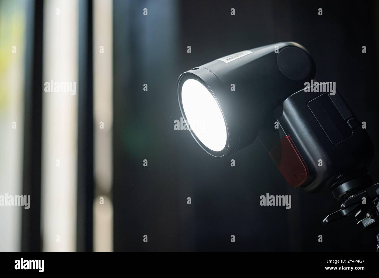 Gros plan d'un flash de photographie professionnel, doté d'une tête d'éclairage ronde et d'un support robuste. Le flash est allumé, émettant un blanc brillant Banque D'Images