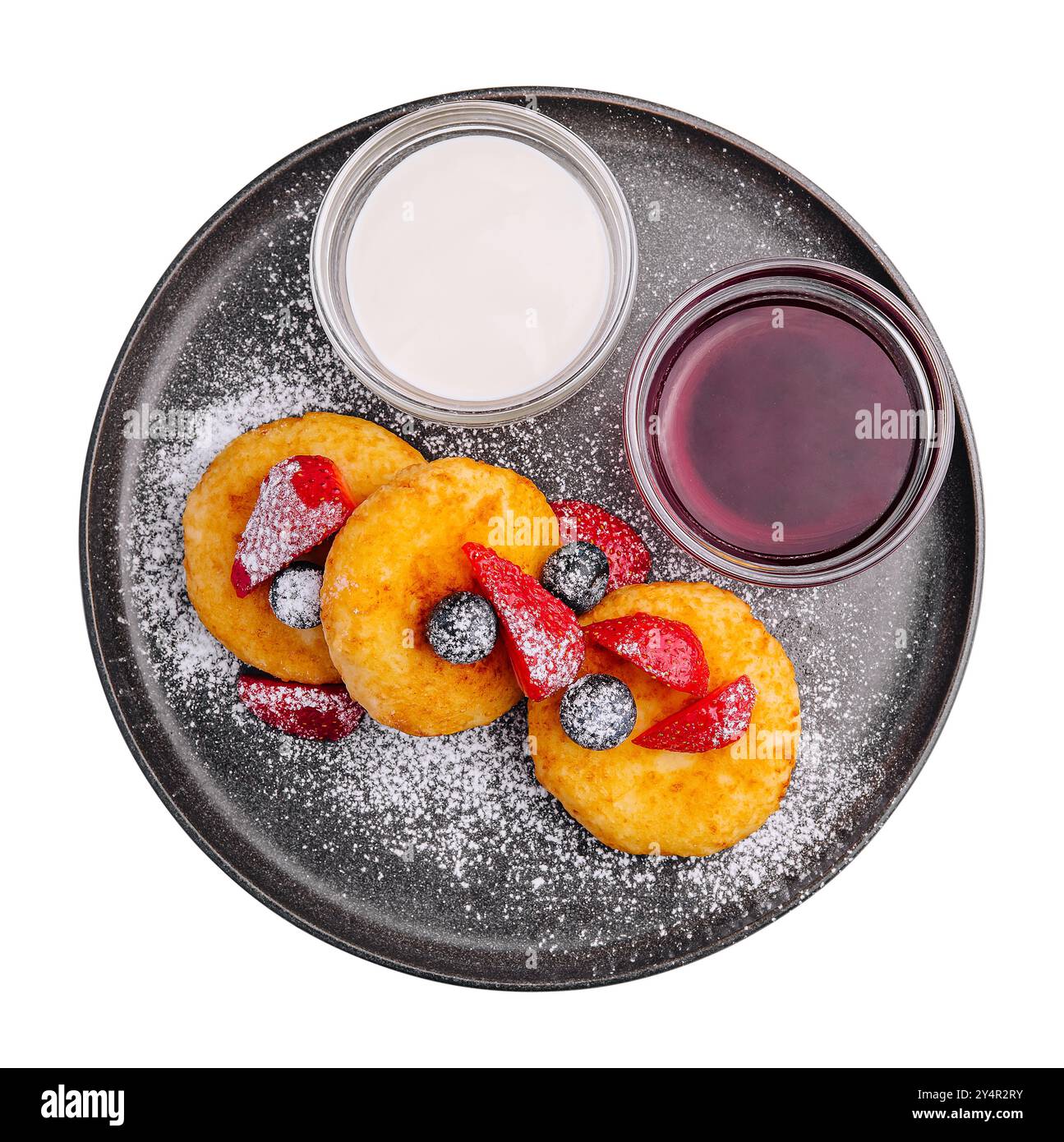 Crêpes au fromage cottage avec baies, sucre en poudre, confiture et crème sure sur plaque noire sur fond blanc Banque D'Images