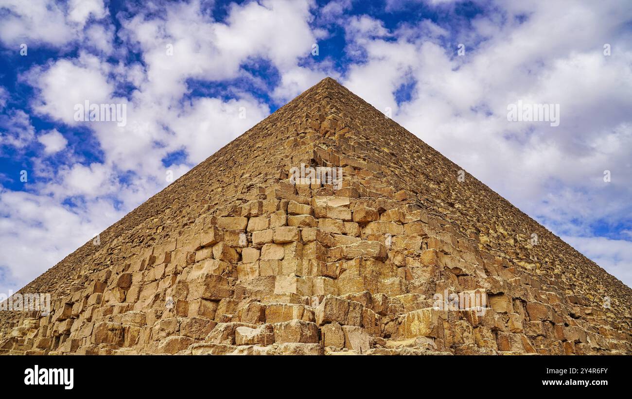 Vue parfaitement symétrique de la Grande Pyramide de Khoufou avec ses blocs de calcaire jaune contre un ciel nuageux sur le plateau de Gizeh Banque D'Images