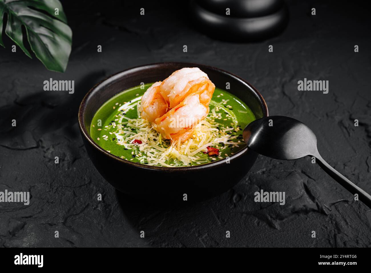 Présentation gourmande de soupe de crevettes aux épinards ornée de garnitures dans un bol sombre sur une surface texturée Banque D'Images