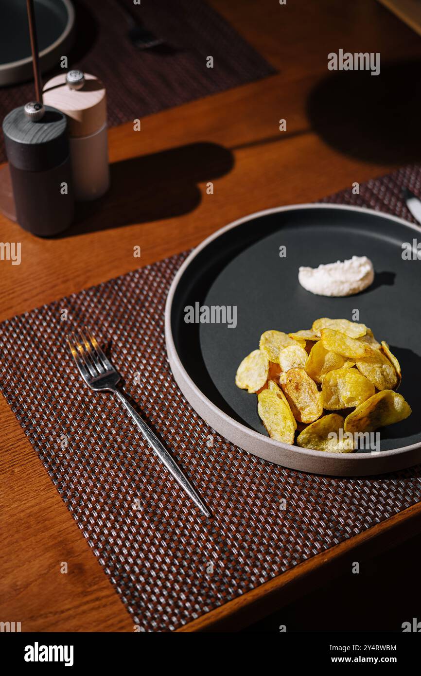 Table à manger moderne avec une assiette de chips artisanales et un côté de trempette dans une ambiance de restaurant chic Banque D'Images