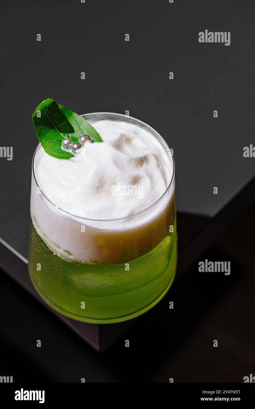 Cocktail vert avec mousse de blanc d'oeuf et garniture de feuille de basilic est debout sur le comptoir du bar Banque D'Images