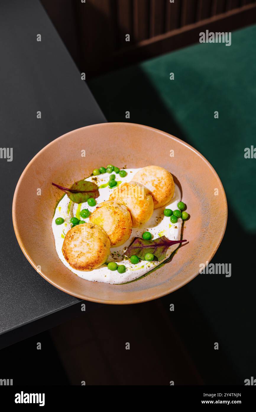 Côtelettes de poulet avec petits pois verts et sauce blanche couchées dans une assiette beige sur une table sombre Banque D'Images