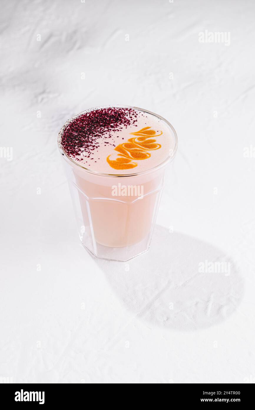 La boisson au lait rose lune servie dans un verre transparent avec un motif sur le dessus se tient debout sur un fond blanc jetant une ombre Banque D'Images