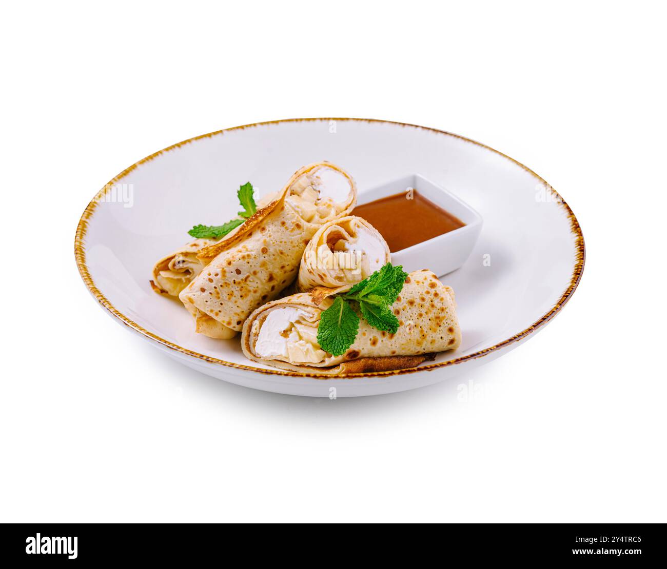 Crêpes fines avec fromage cottage et tranches de banane décorées de feuilles de menthe couchées sur une assiette blanche avec sauce sucrée Banque D'Images