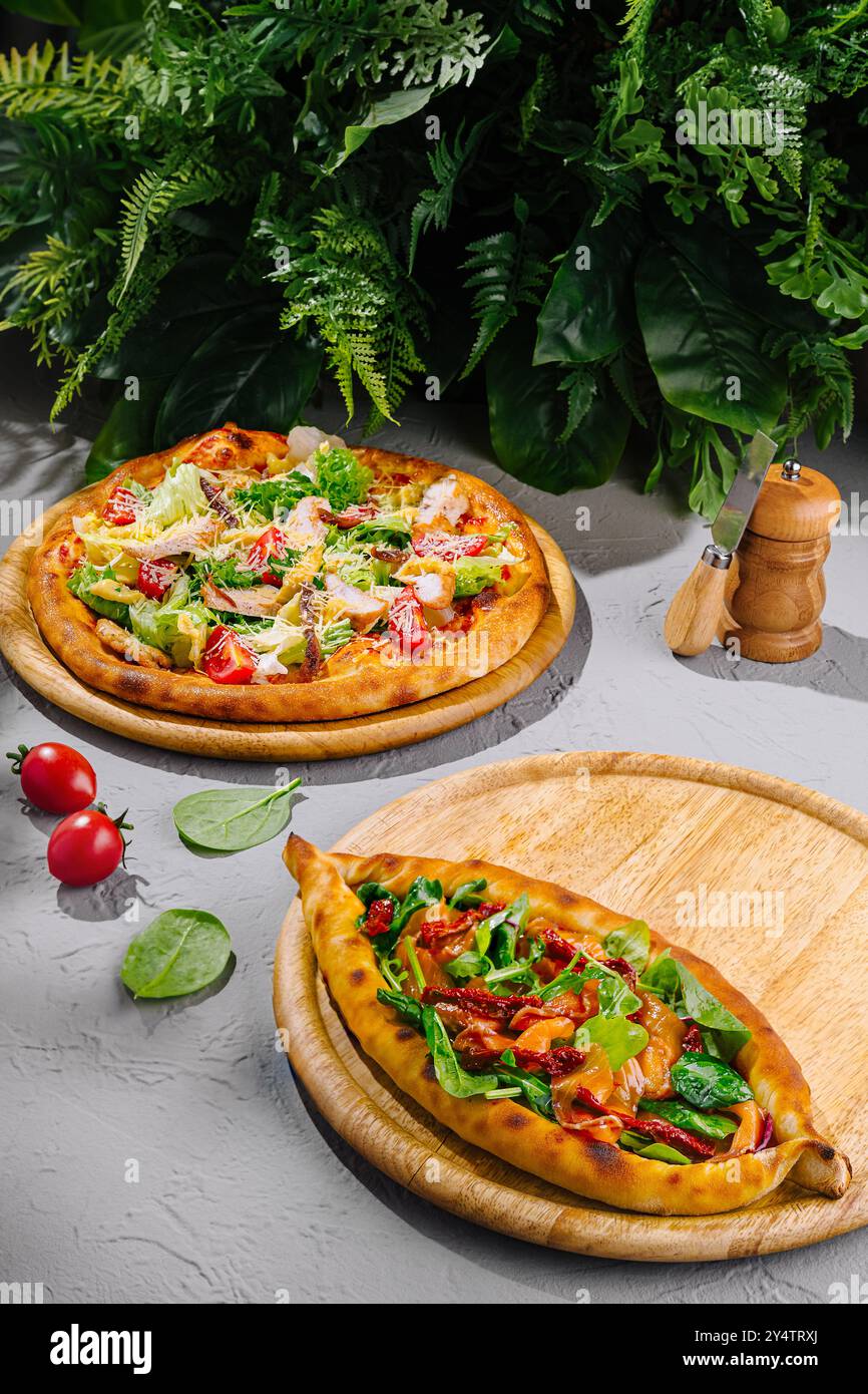 Pizza salade César et pide turque avec tomates séchées au soleil et épinards couchés sur des planches de bois sur une table grise Banque D'Images