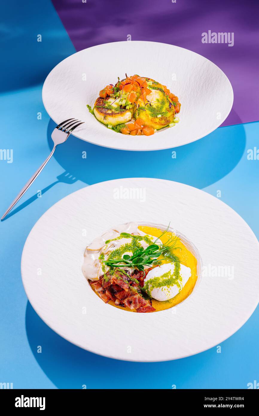 Deux plats exquis sont servis sur des assiettes blanches, mettant en valeur un arrangement vibrant de couleurs et de textures sur un fond bleu et violet vif Banque D'Images