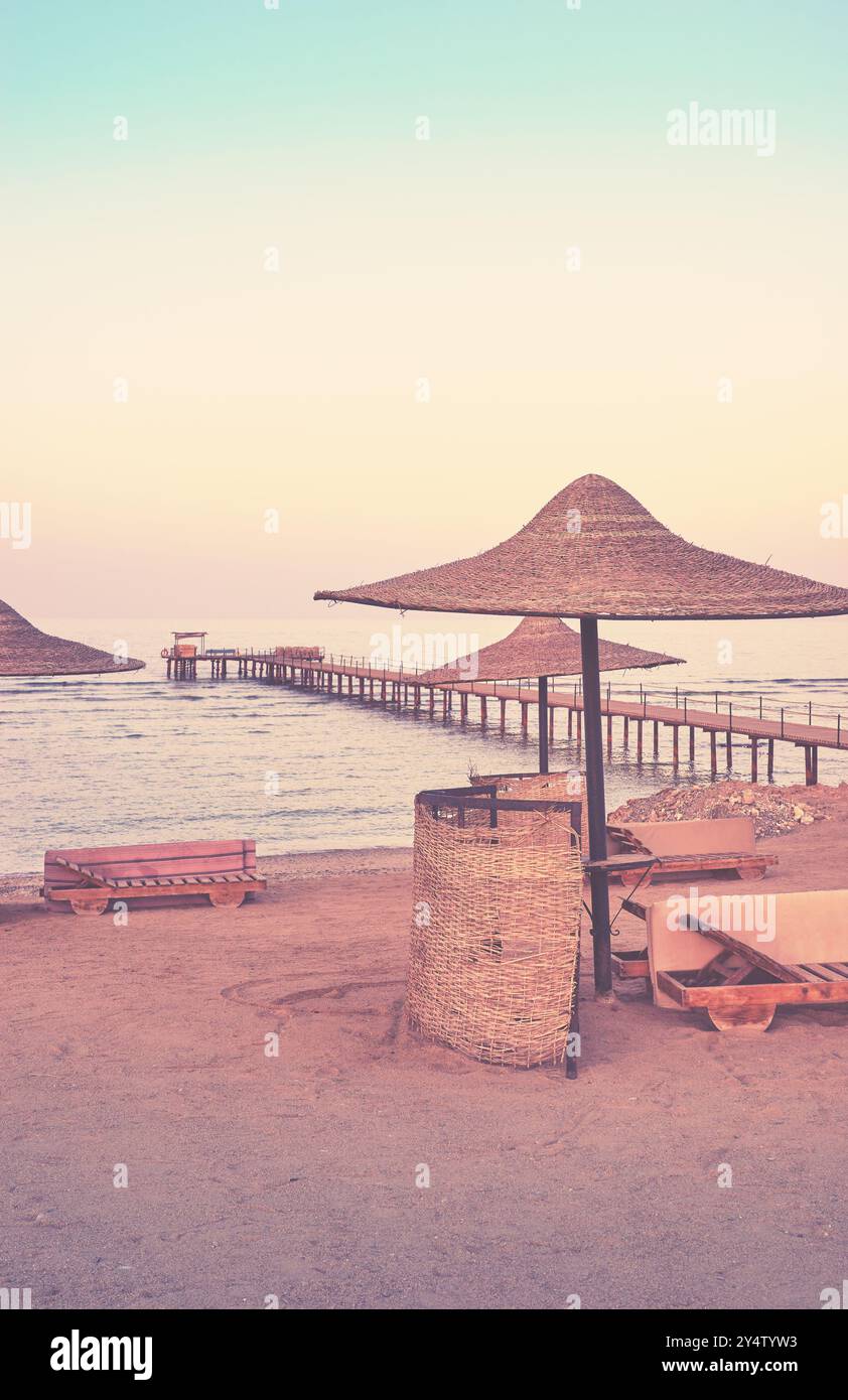 Plage vide avec parasol de jetée et chaises longues au coucher du soleil, tonification de couleur appliquée. Banque D'Images