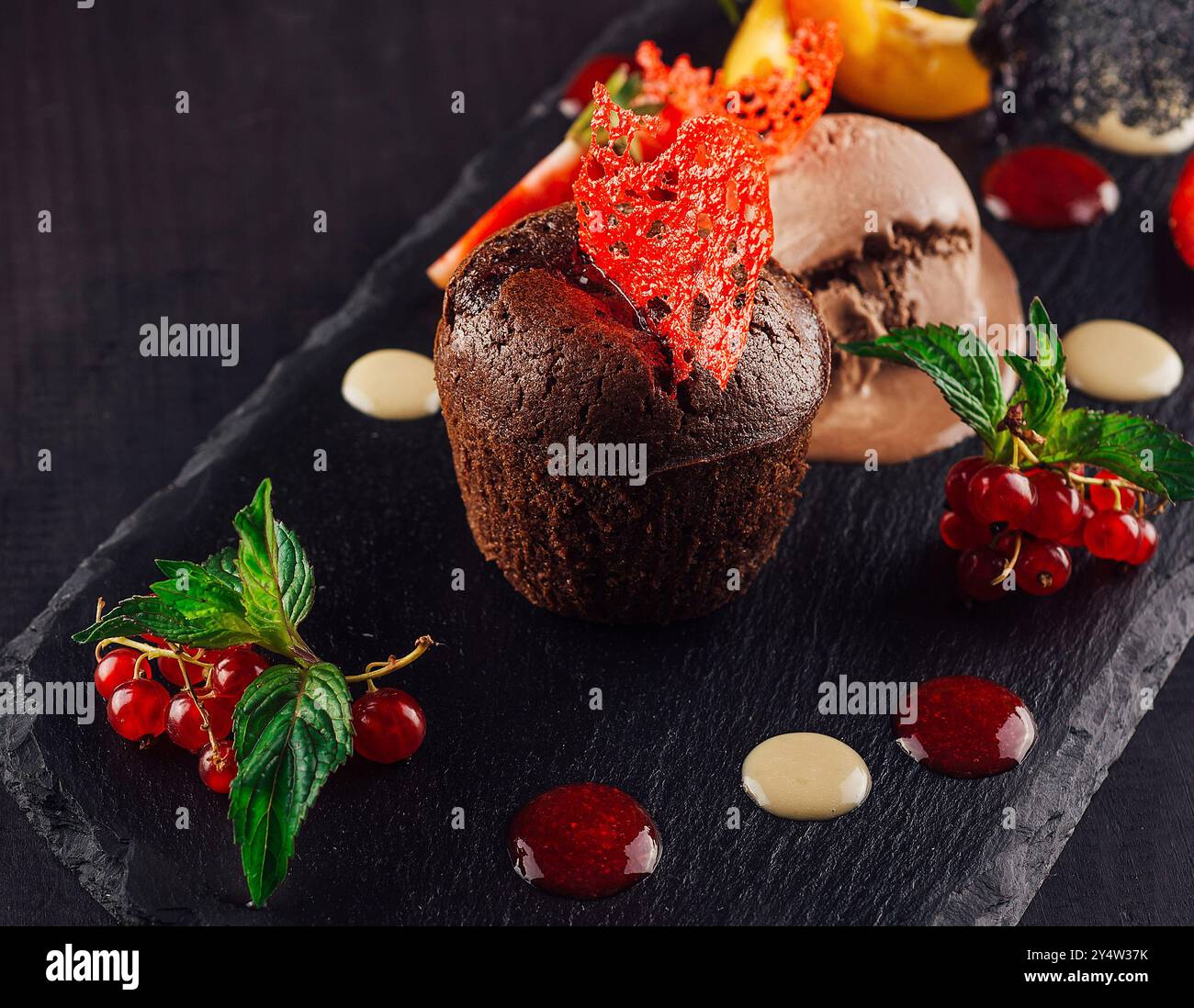 Gâteau de lave au chocolat servi sur une assiette en pierre noire avec une boule de glace, garnie de groseilles rouges, de menthe et d'une fraise Banque D'Images