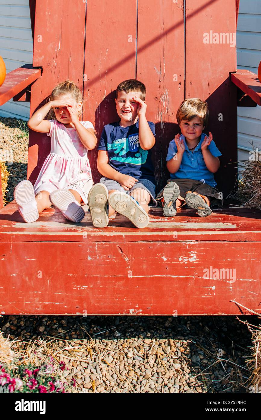 Trois enfants sont assis sur une grande chaise rouge Banque D'Images