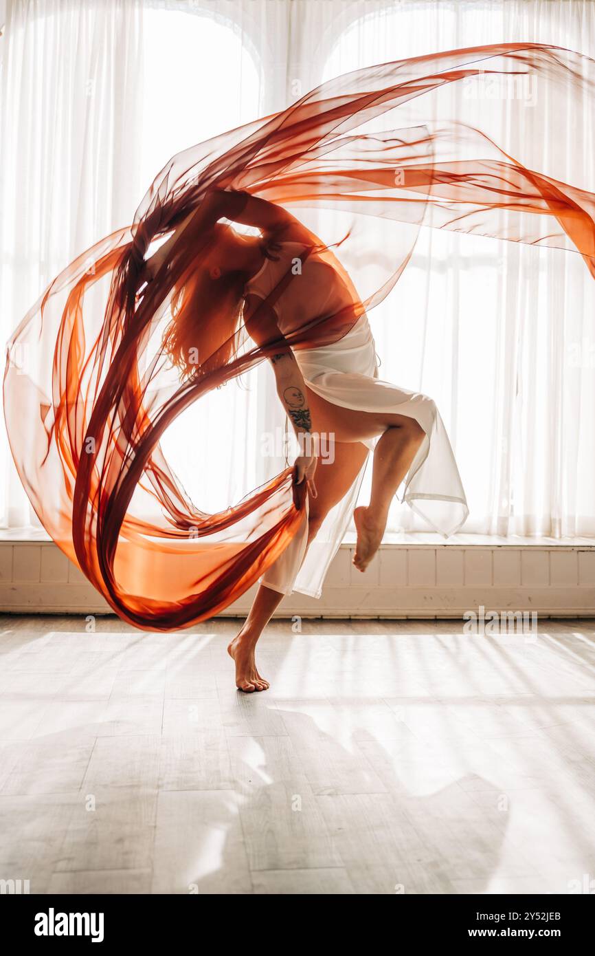 Danseuse de ballet avec tissu rouge fluide voûtant gracieusement Banque D'Images