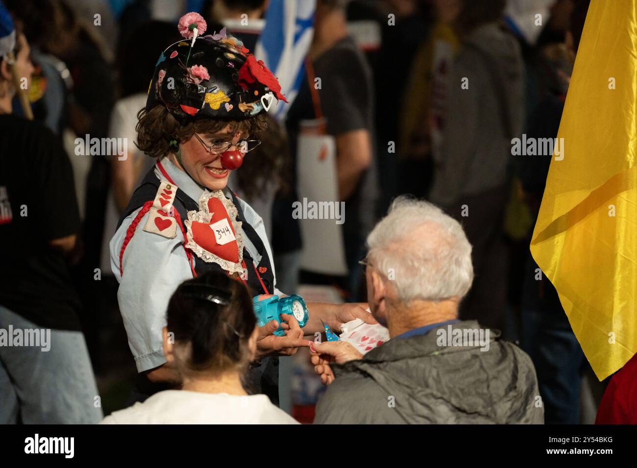 Une personne habillée en clown joyeux tend un autocollant à un participant à une manifestation pour la libération des otages le 14/9/24 sur la place Paris, Jérusalem Banque D'Images