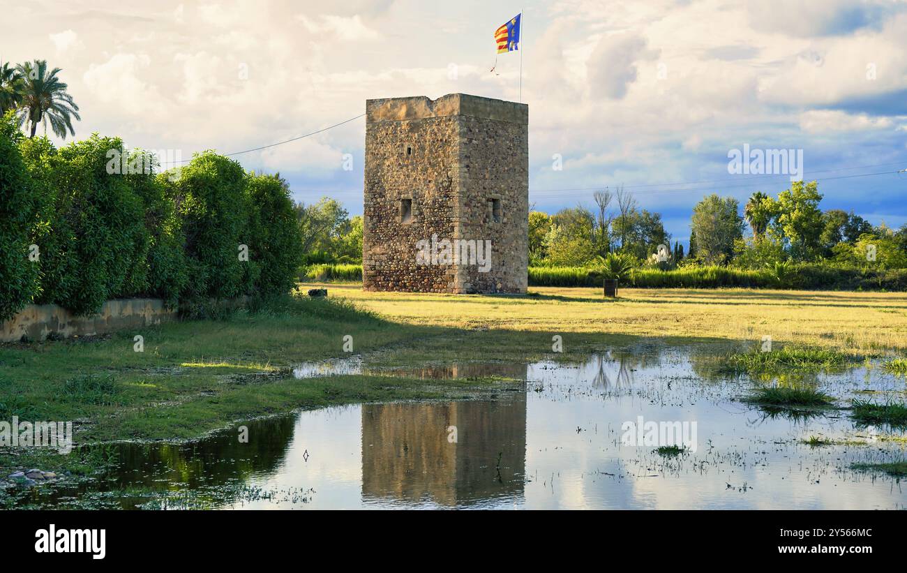 Une tour de pierre reflétée dans un lac calme entouré de végétation. L'image met en valeur la beauté de l'architecture historique en harmonie avec la nature. Banque D'Images