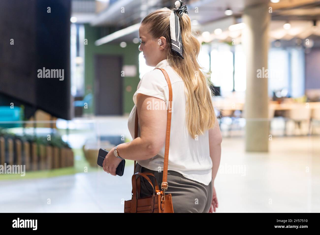 Marchant dans le bureau, femme tenant un smartphone et un sac à main, se concentrant sur l'avenir Banque D'Images