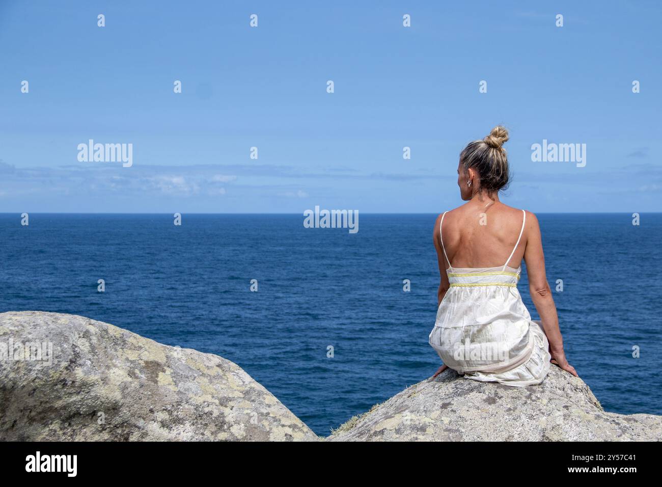 Femme blonde avec ses cheveux en haut portant une robe blanche sur une falaise par la mer faisant des gestes avec ses mains. Copier l'espace Banque D'Images