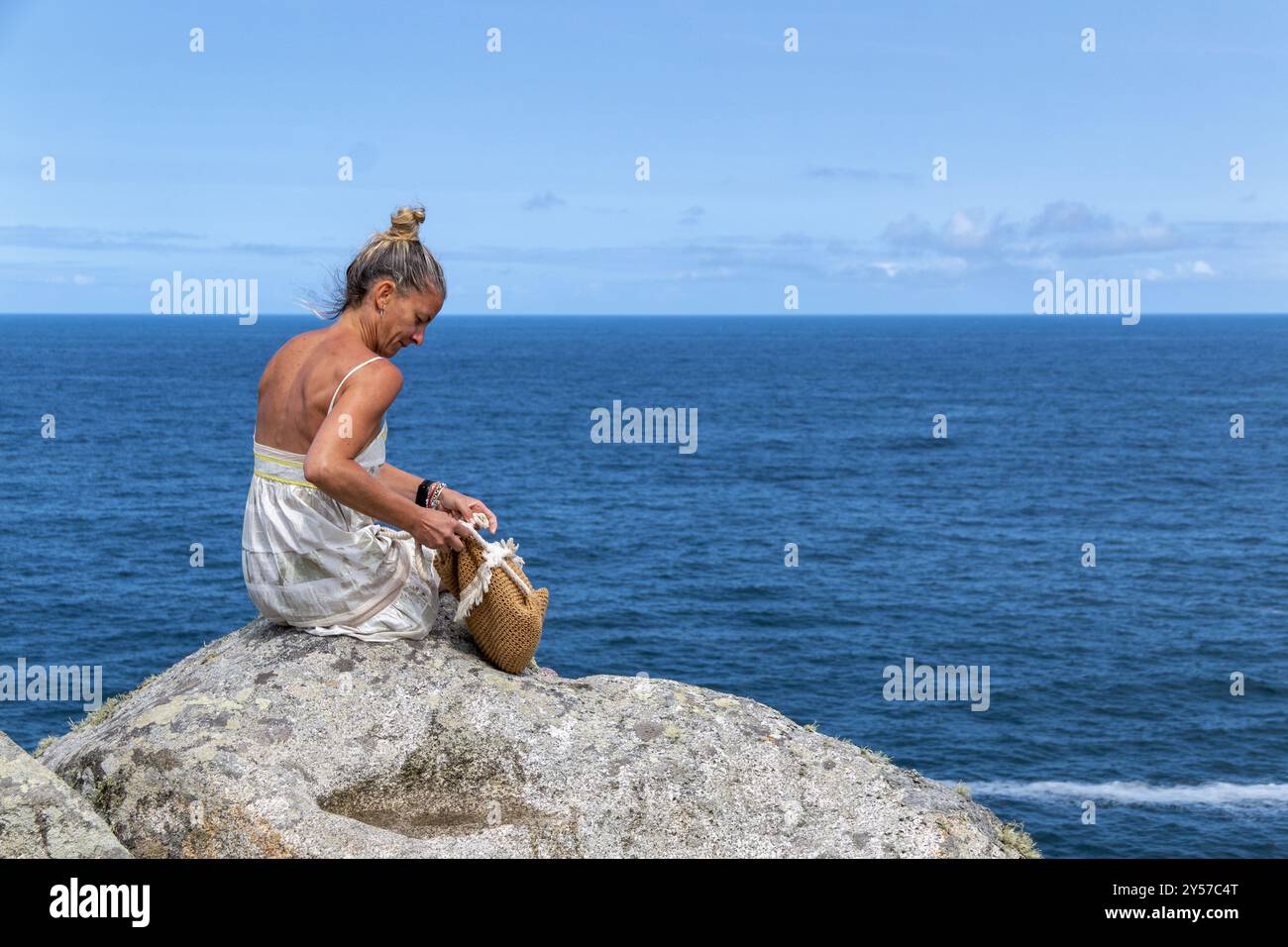 Femme blonde avec ses cheveux en haut portant une robe blanche sur une falaise par la mer faisant des gestes avec ses mains. Copier l'espace Banque D'Images