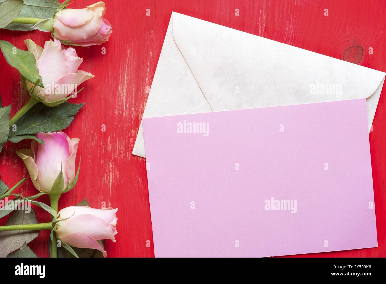 Idée de carte de vœux avec un papier rose sur une enveloppe fermée, entourée de roses rouges sur un fond de bois. Un concept pour le jour de la mère, et la saint valentin Banque D'Images