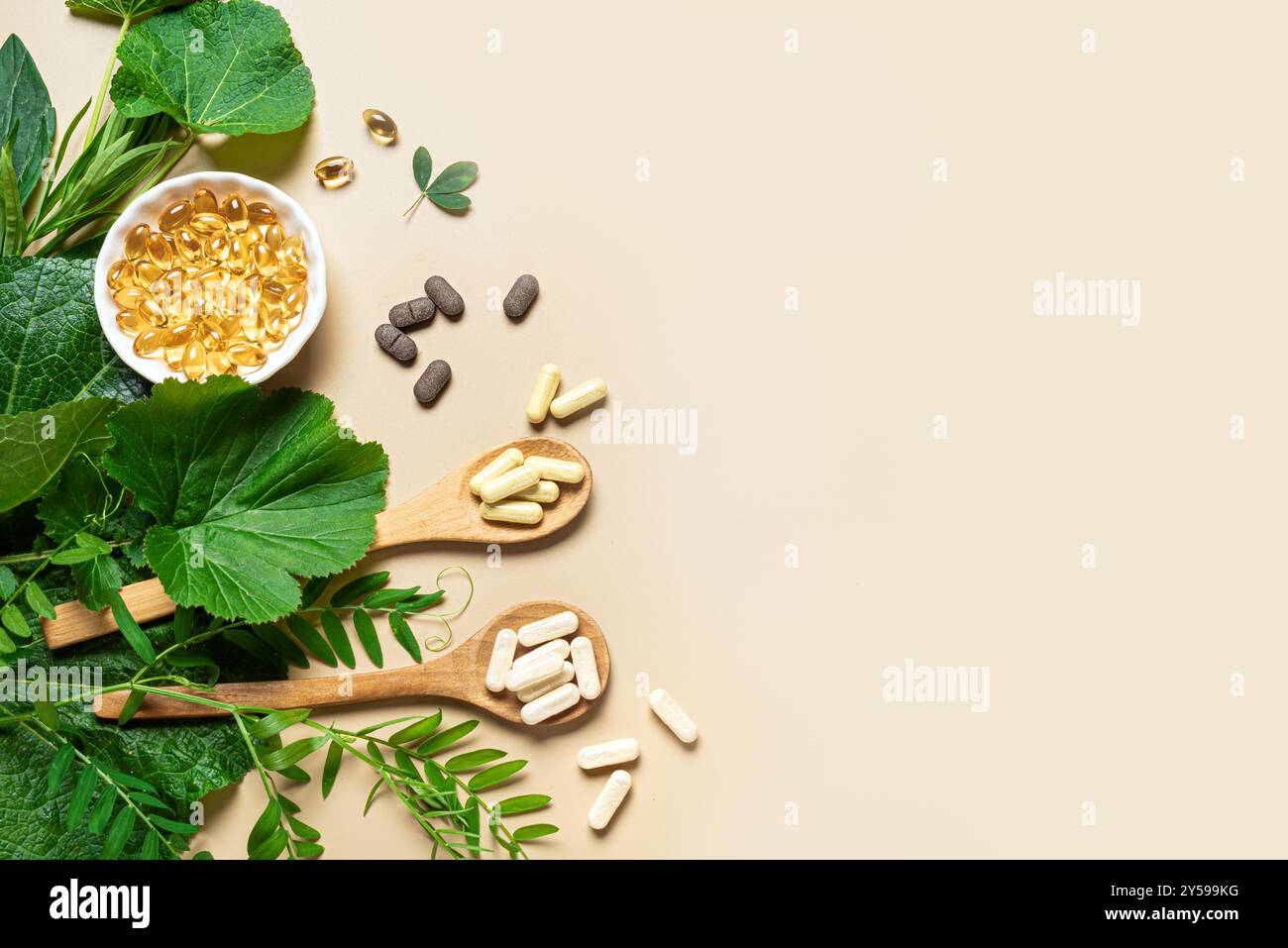 Vitamines naturelles, suppléments à base de plantes et feuilles vertes sur fond beige, vue de dessus, espace de copie. Diverses capsules et pilules biologiques végétaliennes. Banque D'Images
