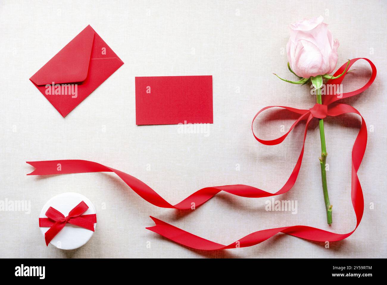 Carte d'anniversaire avec une boîte cadeau mignonne, une rose rose nouée avec un ruban rouge et un noeud, une enveloppe et une carte de message vierge, sur un fond de tissu vintage Banque D'Images