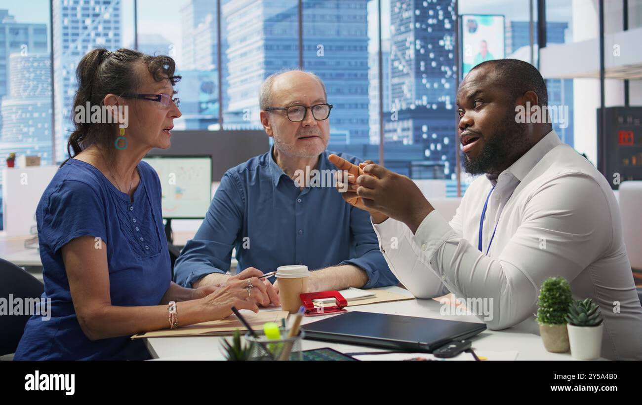 Réunion de deux personnes âgées avec un expert financier pour explorer des stratégies de retraite complètes, y compris l'épargne, les régimes de retraite et les placements. Examiner les options pour sécuriser les finances. Caméra B. Banque D'Images