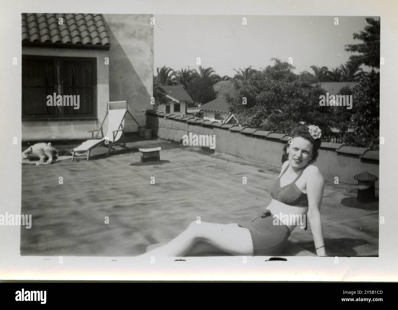 Une femme se détend dans un maillot de bain deux pièces sur un toit, profitant de la journée ensoleillée avec des palmiers en arrière-plan. Cette photo capture un moment insouciant au cours de ce qui semble être un après-midi paisible à Los Angeles, en Californie. Banque D'Images