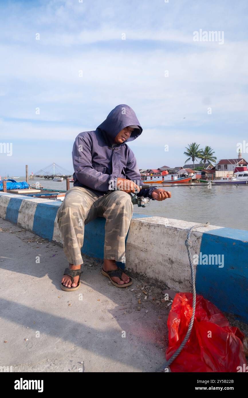 Balikpapan, Bornéo oriental, Indonésie-19 septembre.Un homme est assis sur un mur au bord de l'eau, portant une veste à capuche et des tongs Banque D'Images