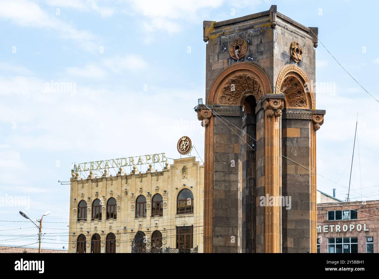 Gyumri, Arménie - 19 juillet 2024 : Monument du 60ème anniversaire de Leninakan et Hôtel Alexandrapol en arrière-plan dans la ville de Gyumri sur somme ensoleillée nuageuse Banque D'Images