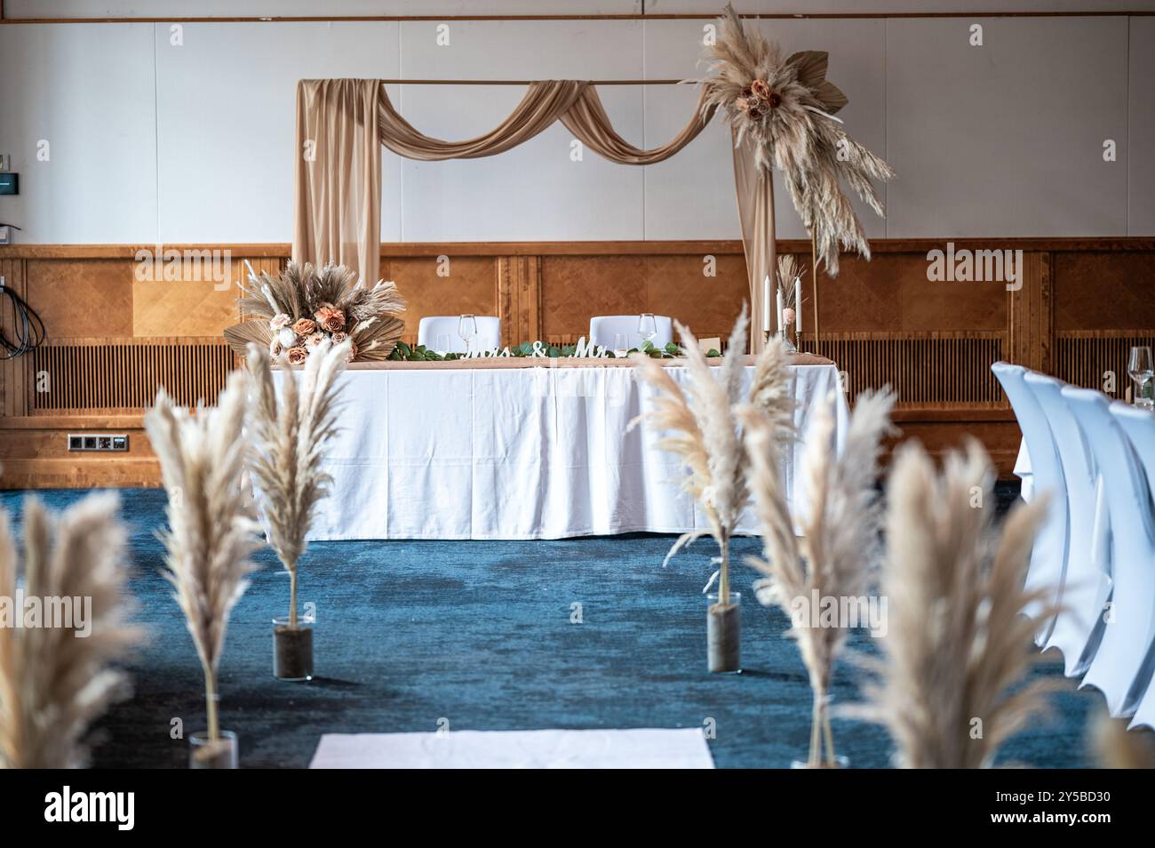 Décoration de mariage. Magnifique lieu d'événement. Table de réception ronde intérieure avec fleurs et chaises. Compositions de fleurs et de plantes dans des stands en bois. Banque D'Images