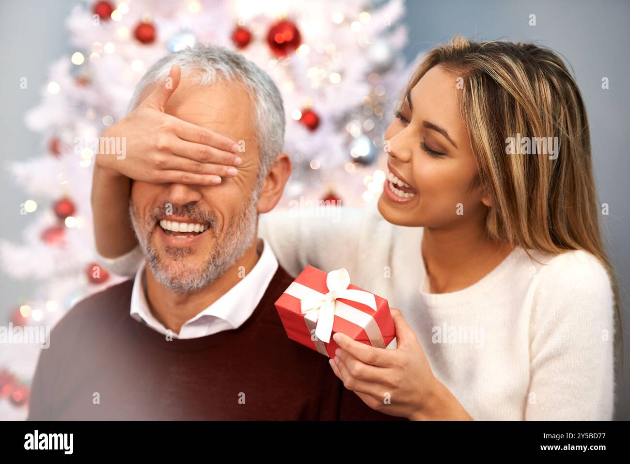 Surprise, cadeau de Noël et femme avec père pour la célébration festive ensemble à la maison de famille. Personne heureuse, secrète et féminine avec boîte cadeau de Noël Banque D'Images