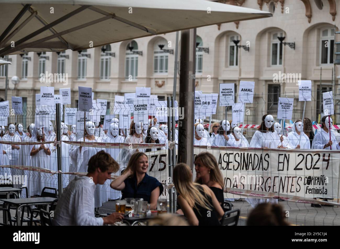 Madrid, Espagne. 21 septembre 2024. Touriste dégustez de la bière sur une terrasse alors qu'un groupe de femmes avec des masques, vêtues de blanc et portant des pancartes portant les noms et l'âge des femmes assassinées en tant que victimes de violence sexiste, rassemblées devant le Parlement espagnol pour dénoncer une manifestation contre les 75 femmes assassinées jusqu'ici cette année en Espagne comme victimes de violence sexiste et de machisme. Crédit : Marcos del Mazo/Alamy Live News Banque D'Images