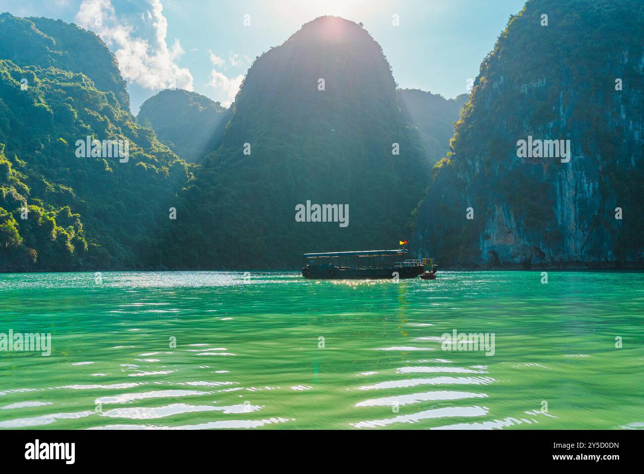 Bateau de pêche vietnamien traditionnel croisière dans la baie de Ha long avec des rayons de soleil sur l'eau bleue immaculée parmi les montagnes. Paysage de rêve des unes de la baie d'Ha long Banque D'Images