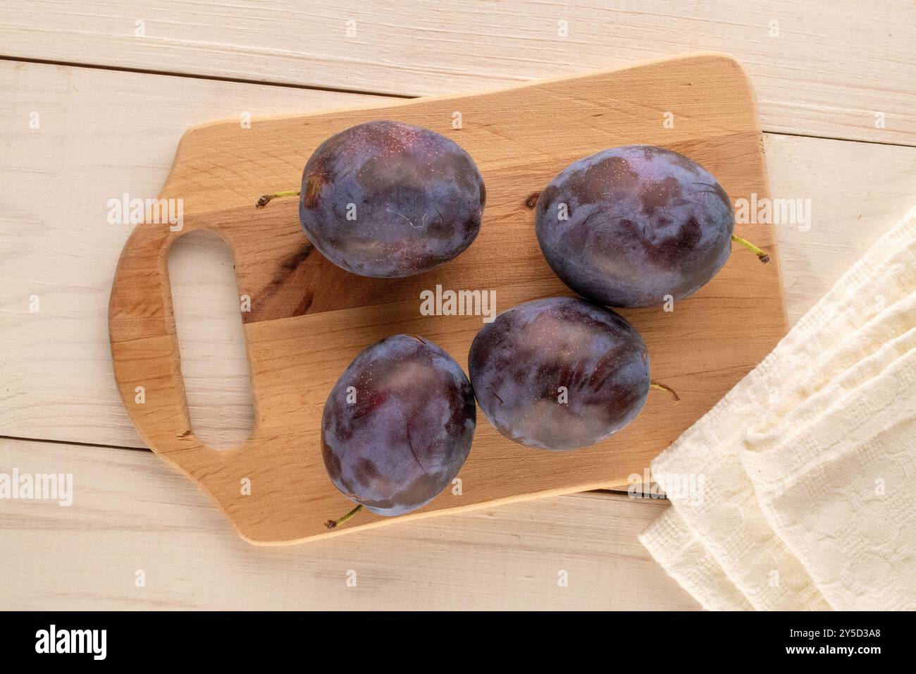 Prunes mûres avec planche à découper en bois sur table en bois, macro, vue de dessus. Banque D'Images