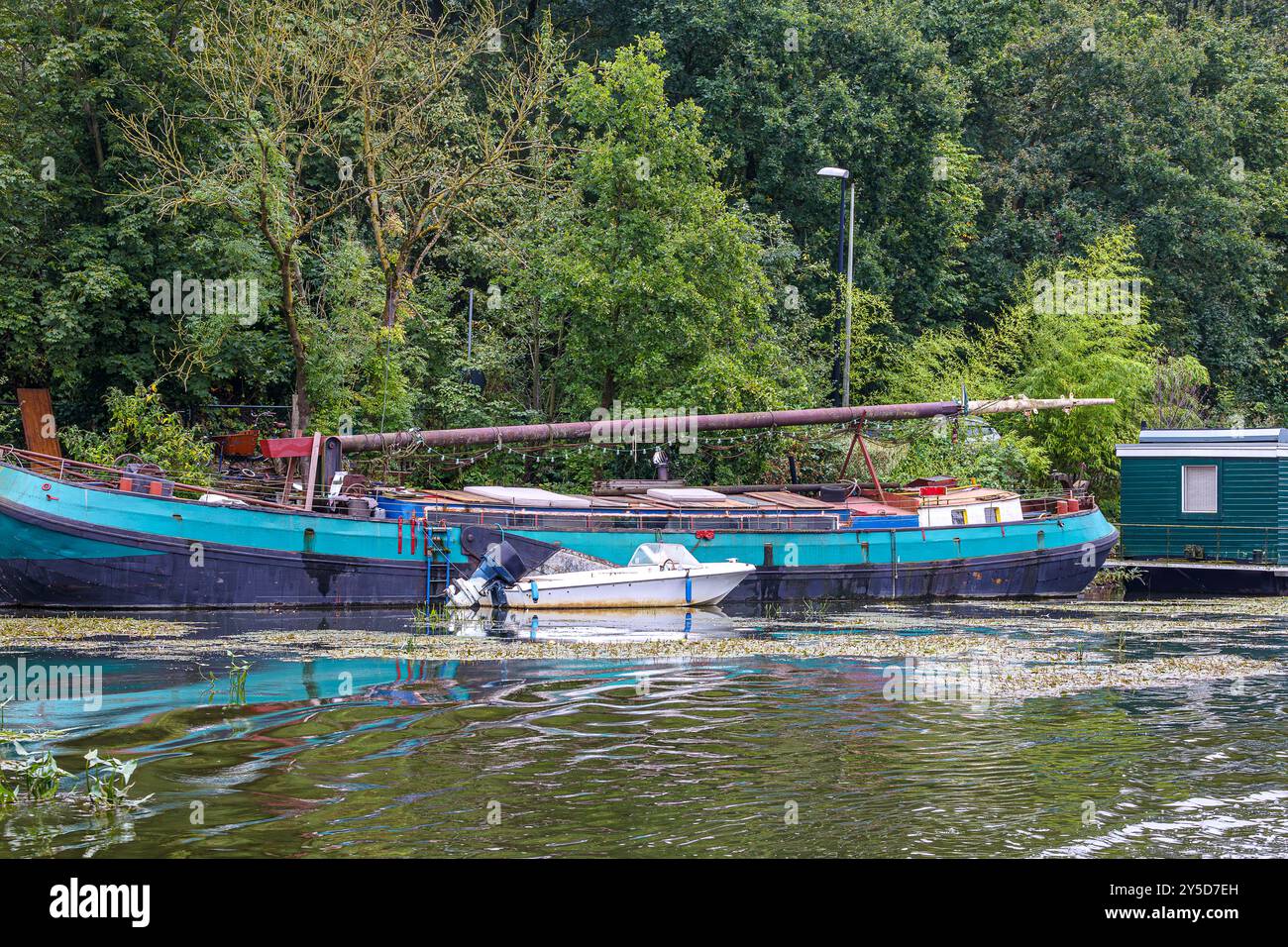 Ancienne barge utilisée comme péniche sur la rive du canal maritime en dehors de la ville de Maastricht, petit bateau, eau avec des plantes aquatiques en surface, arbres feuillus sur backgr Banque D'Images
