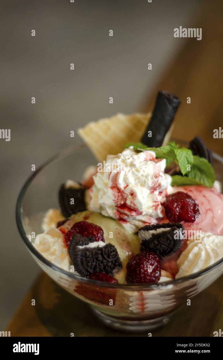 Dessert sundae à la crème glacée à la framboise et à la pistache dans un bol en verre avec des biscuits au chocolat et des baies Banque D'Images