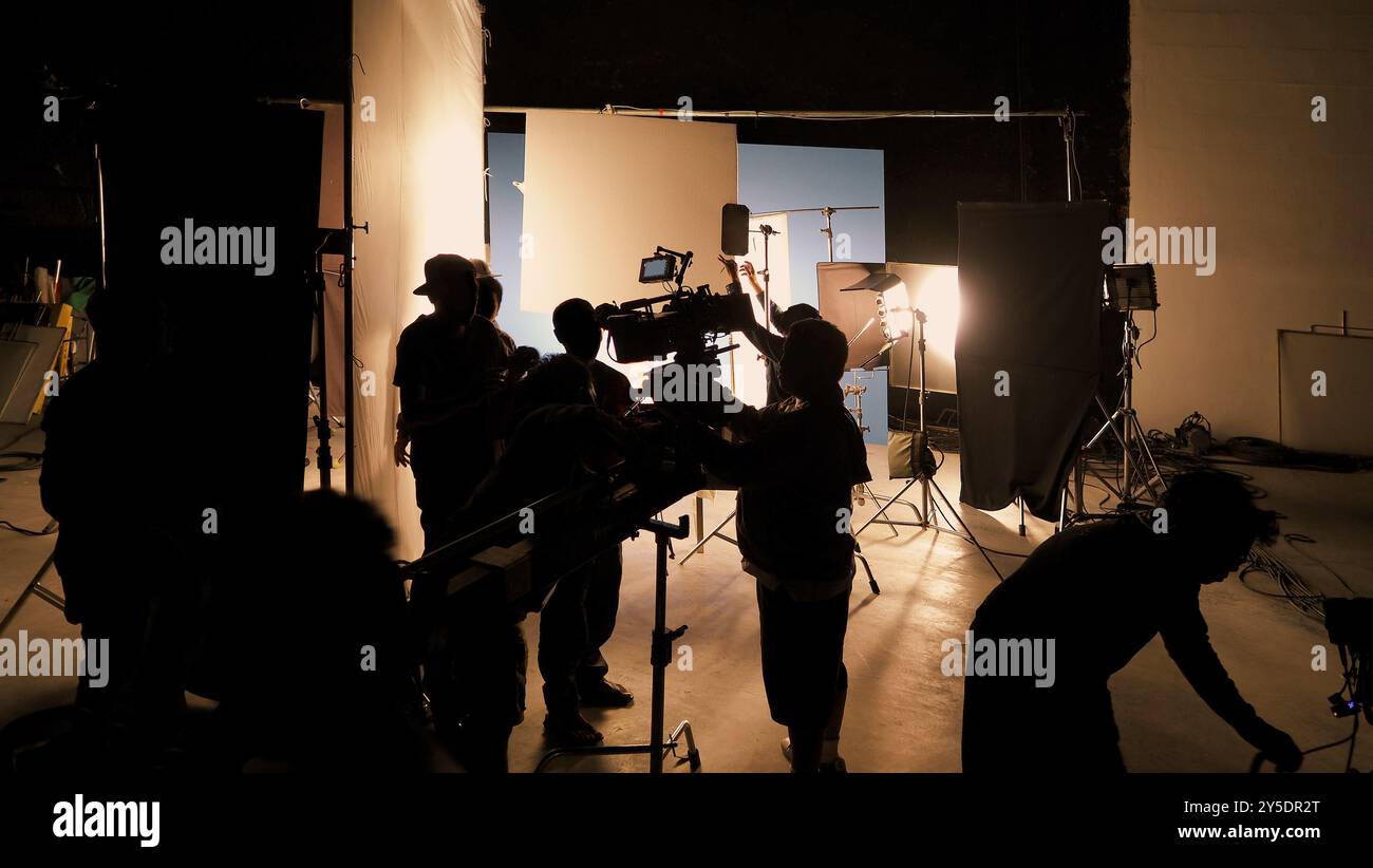 Silhouette des équipes de film et de la caméra vidéo sur une grue de chariot spéciale avec l'équipement de lumières de film et l'ensemble d'écran bleu. Production de films dans les coulisses stu Banque D'Images