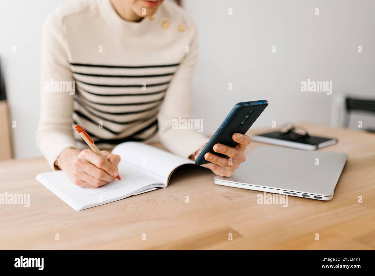 Femme adulte moyenne prenant des notes tout en vérifiant certaines informations sur le téléphone portable Banque D'Images Femme adulte moyenne prenant des notes tout en vérifiant certaines informations sur le téléphone portable Banque D'Images