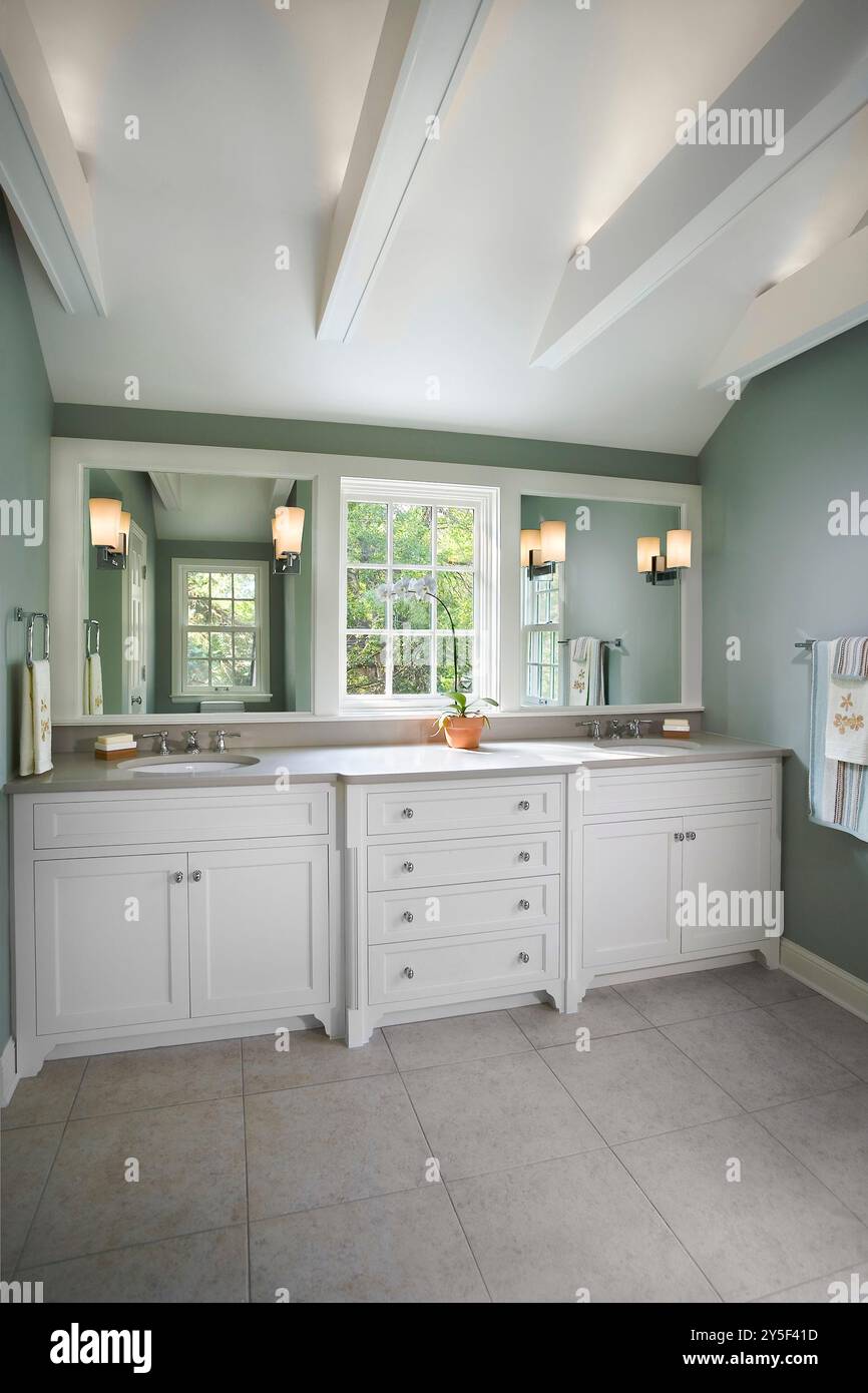 Belle salle de bain avec lavabo double blanc avec fenêtre entre deux miroirs et poutres de support blanches au plafond Banque D'Images