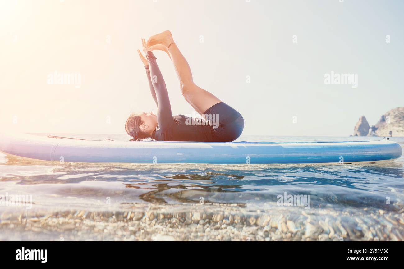 Yoga Paddleboard exercice Ocean Man pratiquer le yoga sur une planche à paddleboard dans l'océan au coucher du soleil Banque D'Images