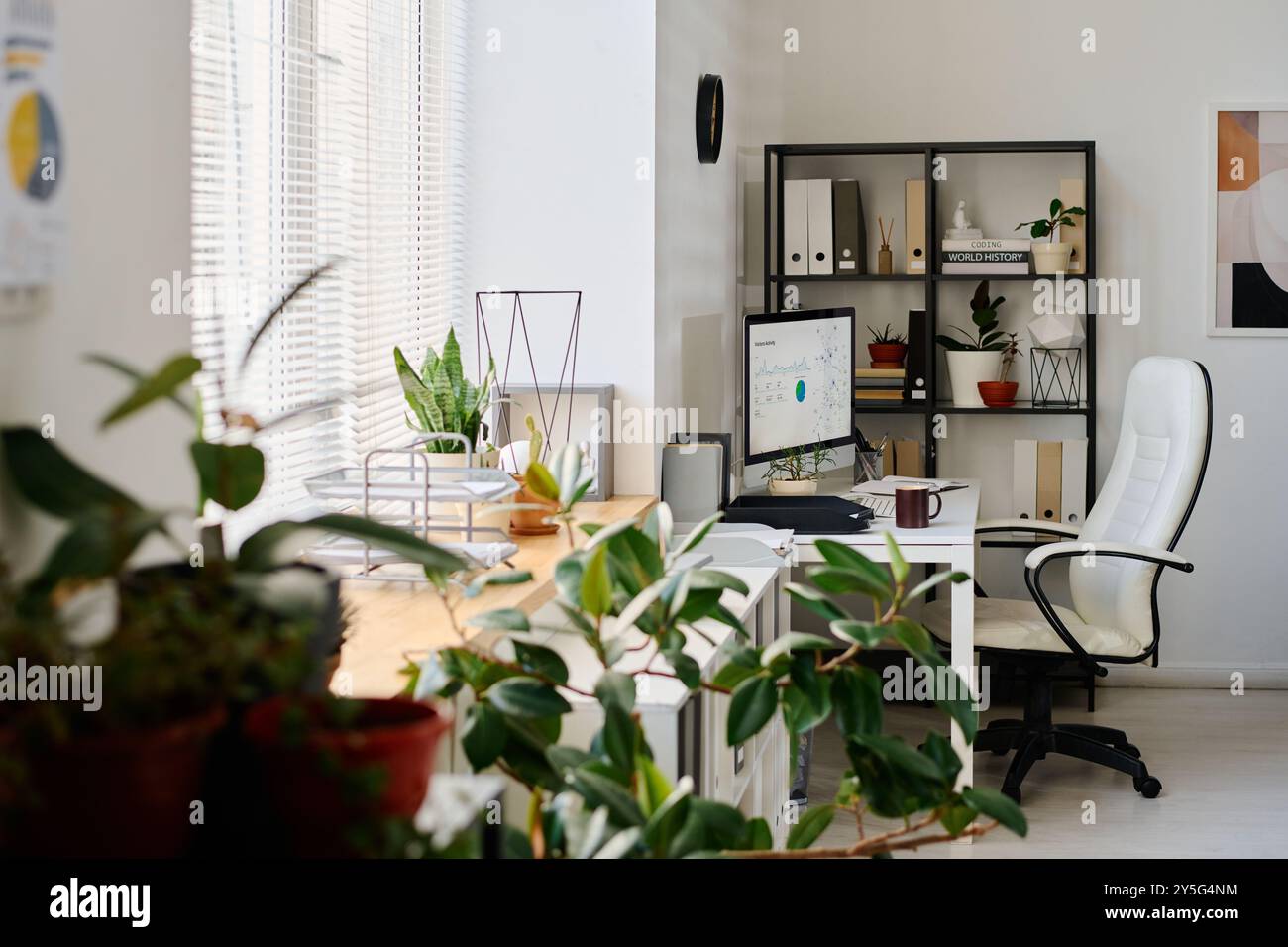Bureau à domicile lumineux avec mobilier blanc, décor moderne et plantes vertes, avec ordinateur et étagères organisées avec divers articles Banque D'Images