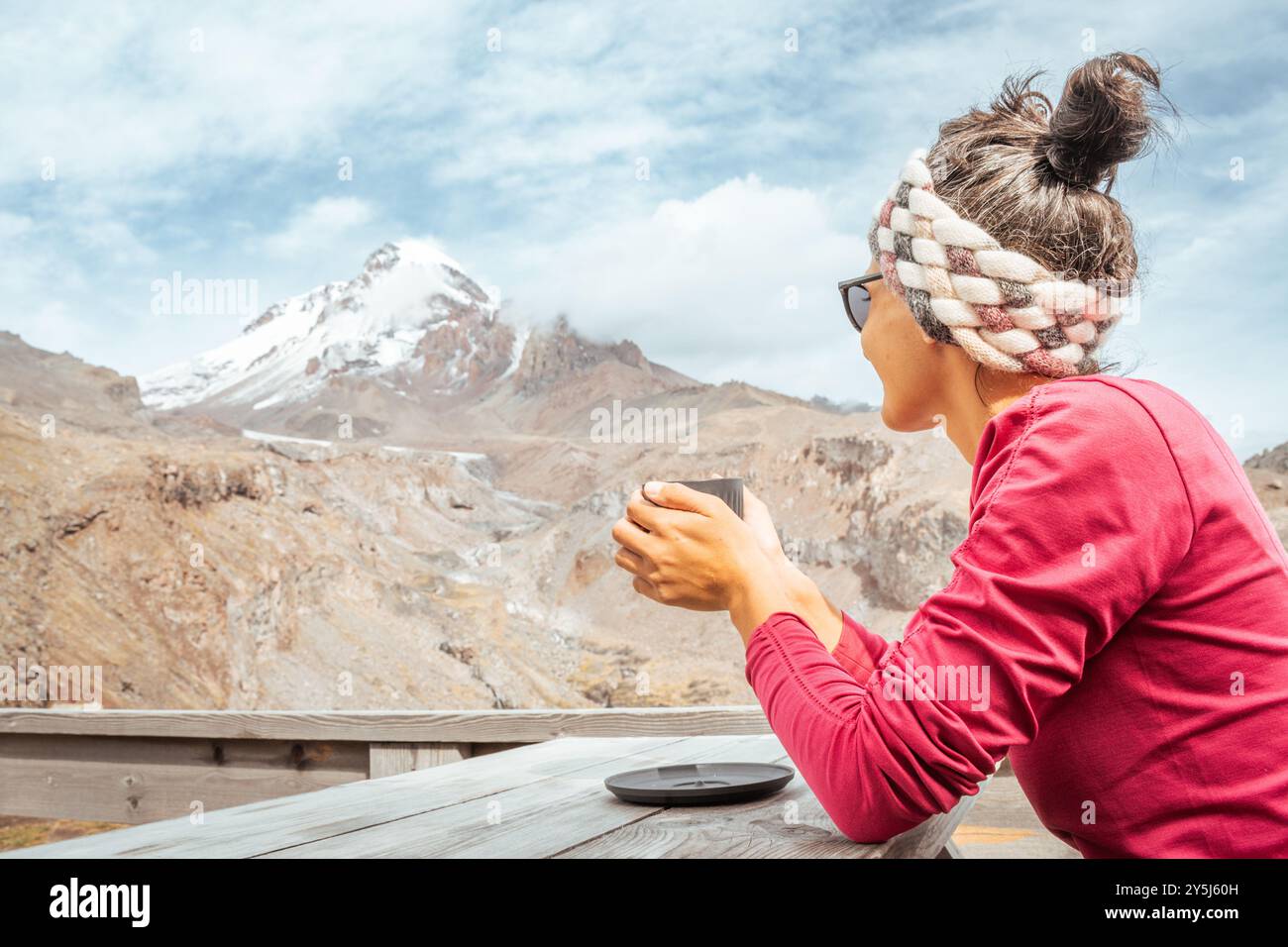 Caucasien jeune femme touristique heureuse assise dans le café de montagne tenir tasse de chocolat chaud regarder Kazbek panorama de pic de montagne dans le parc national de Kazbegi. Tr Banque D'Images