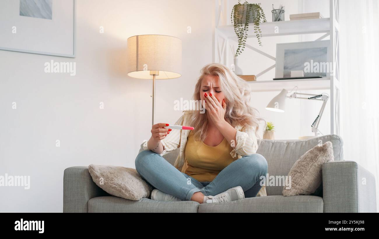 Grossesse non planifiée. Femme désespérée. Triste émotion. Contrarié la dame qui pleure résultat du test assis canapé lumière intérieur de la pièce. Banque D'Images