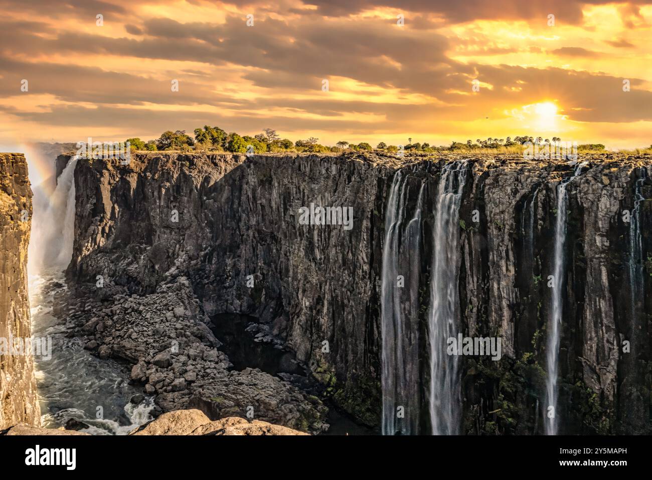 Une vue impressionnante des chutes Victoria au cours d'un majestueux coucher de soleil doré, mettant en valeur l'étendue à couper le souffle de la puissante cascade, ses falaises escarpées et son lu Banque D'Images